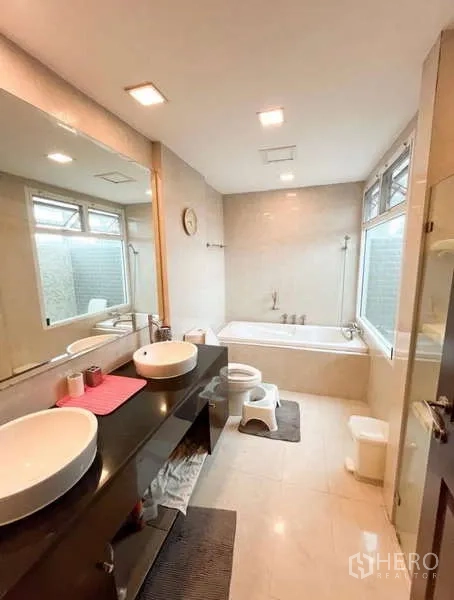 Detached House for rent in Bang Phli, Samut Prakan - Bright bathroom with double vessel sinks, long mirror, bathtub and large windows with neutral tiles.
