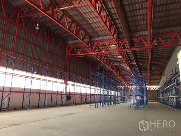 คลังสินค้า ให้เช่าในBang Na, Bangkok - ภายในโกดังกว้าง มีชั้นวางพาเลทสีน้ำเงินหลายแถว ใต้โครงหลังคาเหล็กสีแดง