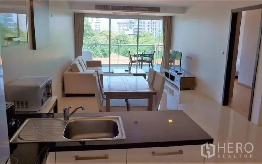 Condominium for sale in Bang Lamung, Chon Buri - Open-plan living and dining area with large windowed balcony and green city views, seen from the kitchen.