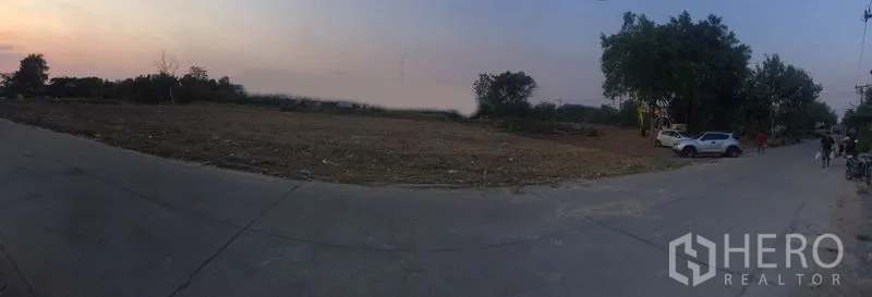 Land for rent in Lam Luk Ka, Pathum Thani - Panoramic view of a cleared corner land plot with paved road access at sunset in Lam Luk Ka.