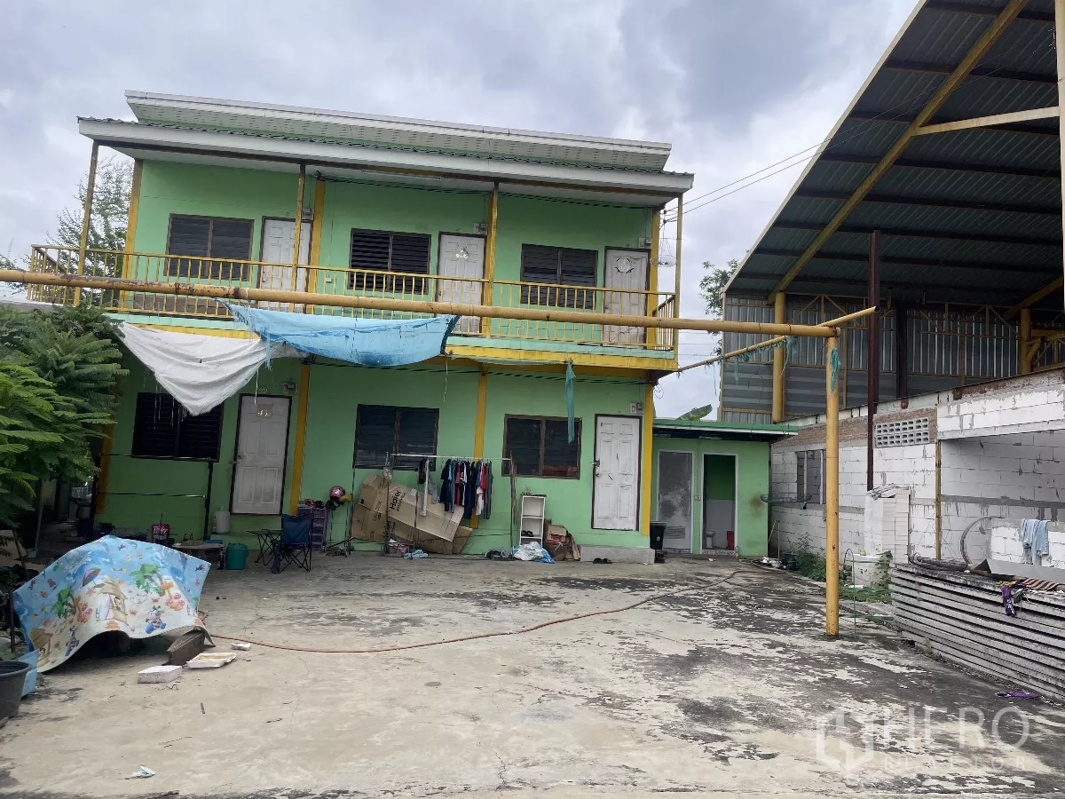 工厂 出售在Bang Bua Thong, Nonthaburi - 两层员工宿舍楼，绿色外墙，旁有硬铺院坝与棚屋。