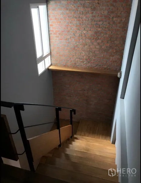 联排别墅 出售在Wang Thonglang, Bangkok - 楼梯为木踏步与金属扶手，旁有窗户和外露砖墙。