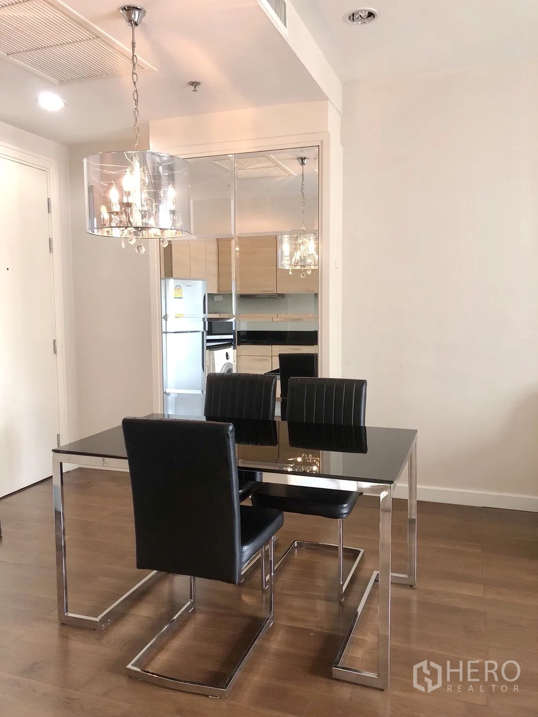 公寓 出租在Pathum Wan, Bangkok - 现代用餐区，黑色玻璃餐桌、皮椅与镜面墙，搭配水晶吊灯。