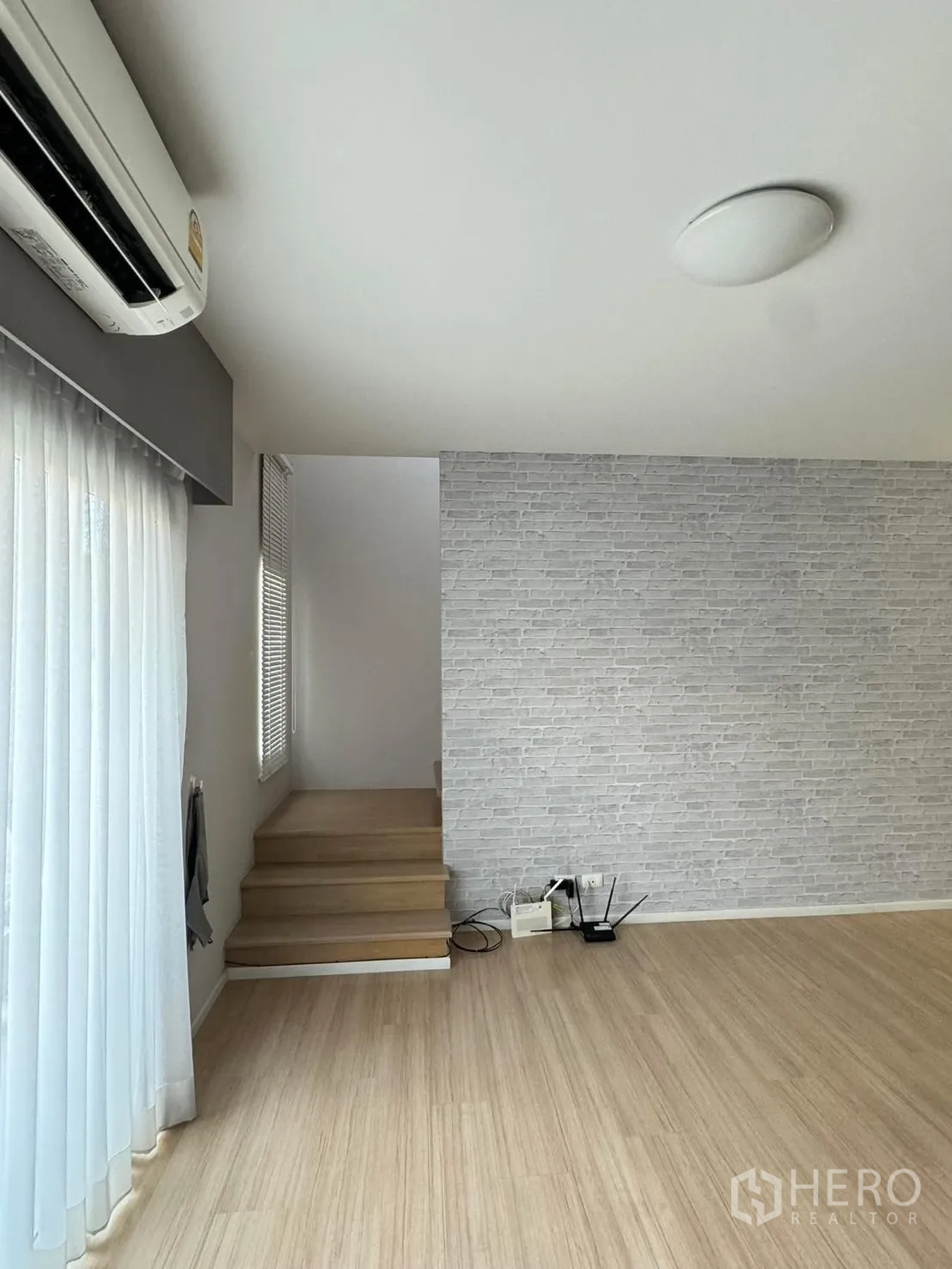 联排别墅 for rent in Suan Luang, Bangkok - 明亮楼梯平台，白色砖纹墙与木阶梯、纱帘。