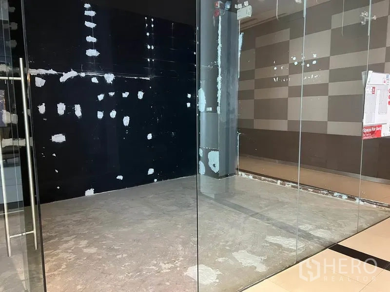 零售空间 出租在Watthana, Bangkok - 透过透明玻璃可见紧凑零售空间，黑色强调墙，外侧为光洁的商场地砖。