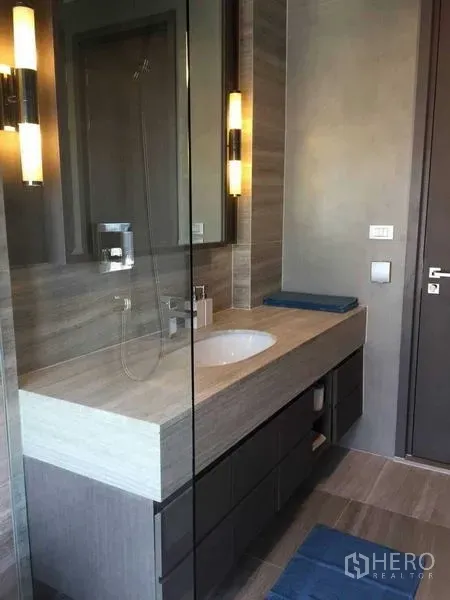 公寓 出租在Bang Rak, Bangkok - 现代卫浴，长台面洗手盆与玻璃淋浴间，暖色灯光。