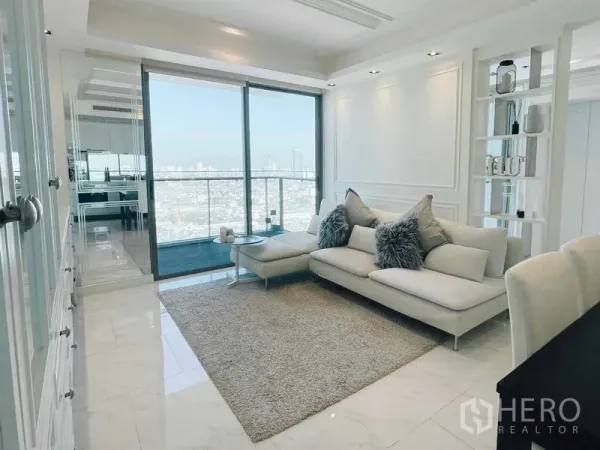 Condominium for rent or sale in Bang Kho Laem, Bangkok - Bright living room with white sectional sofa, rug, and a balcony facing the Bangkok skyline.