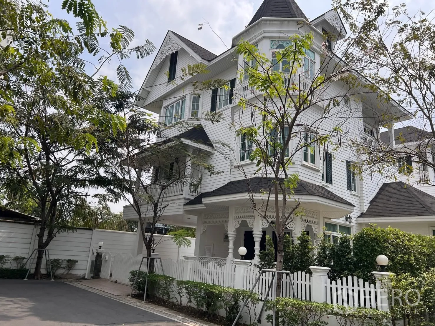 Detached House for rent in Bang Na, Bangkok - White Victorian-style detached house with turret, veranda, and picket fence.