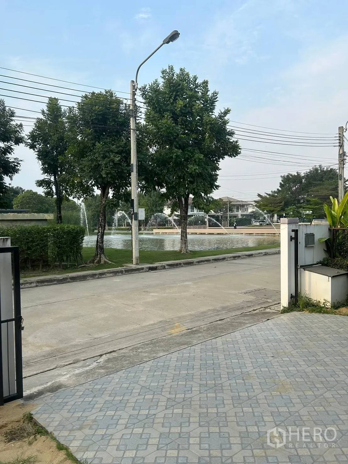 独栋房屋 for rent in Bang Na, Bangkok - 前院与铺砖车道，正对临湖街景与树木喷泉。