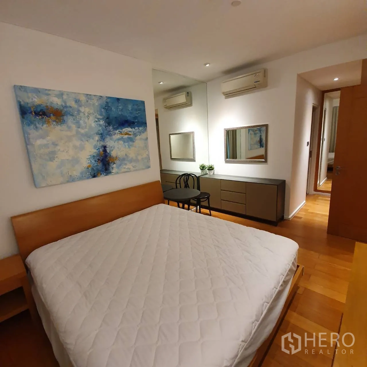 Condominium for rent in Watthana, Bangkok - Bedroom with large bed, mirrored dressing area, wall art and wood flooring.