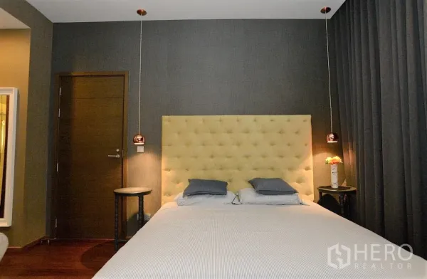 Condominium for rent in Watthana, Bangkok - Cozy bedroom with tufted headboard, dark drapes, side tables, and warm pendant lights.