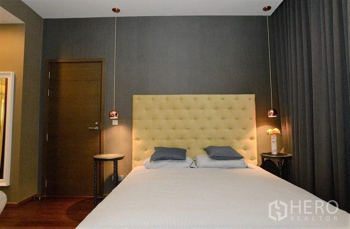 Condominium for rent in Watthana, Bangkok - Cozy bedroom with tufted headboard, dark drapes, side tables, and warm pendant lights.