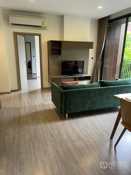 Condominium for rent in Watthana, Bangkok - Living room with green sofa, built-in TV wall, wood floors and doorway to bedroom at Mori Haus condo.