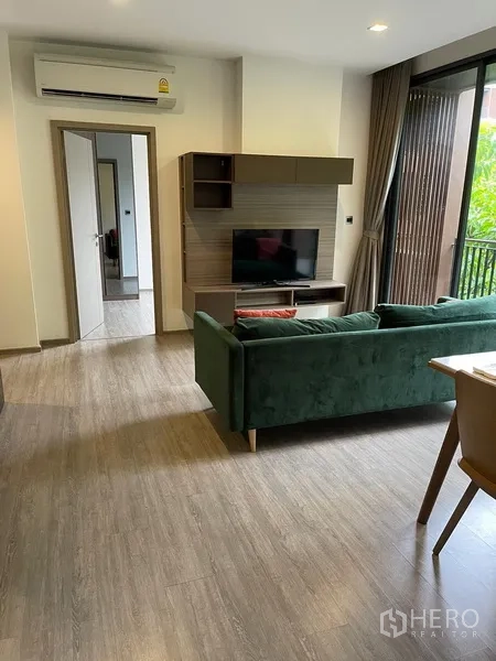 Condominium for rent in Watthana, Bangkok - Living room with green sofa, built-in TV wall, wood floors and doorway to bedroom at Mori Haus condo.