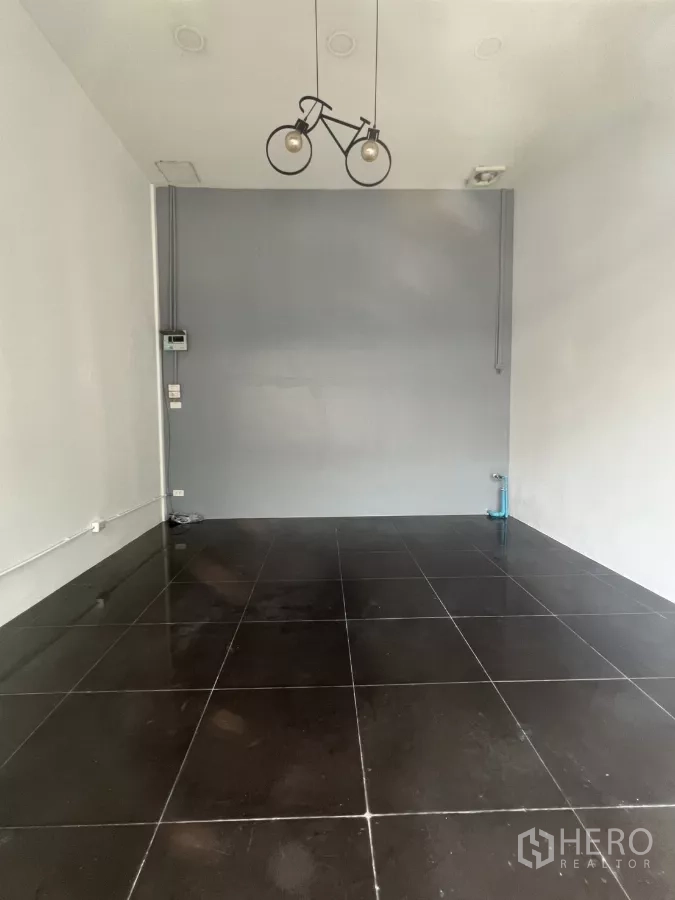 Retail Space for rent in Khlong Toei, Bangkok - Compact retail interior with high ceiling, black tiled floor, and a minimalist grey feature wall.
