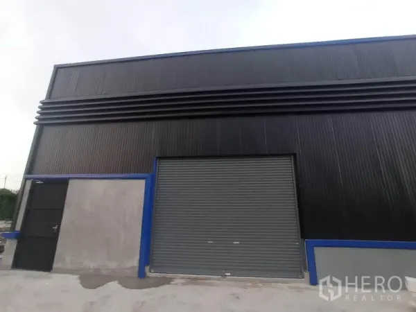 Warehouse for rent in Saphan Sung, Bangkok - Front facade of the warehouse showing a large roller shutter and separate pedestrian entrance.