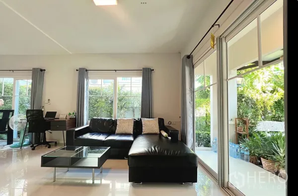 Townhouse for rent or sale in Sai Mai, Bangkok - Living area opening to patio through floor-to-ceiling glass and greenery outside.