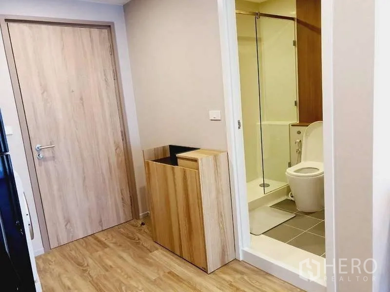 Condominium for rent in Sathon, Bangkok - Entry hallway leading to a bathroom with glass shower and toilet in light wood finishes.