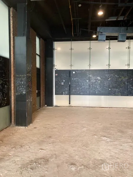 零售空间 出租在Watthana, Bangkok - 店内空间宽敞，地面未完工，黑色特色墙与裸露砖面。