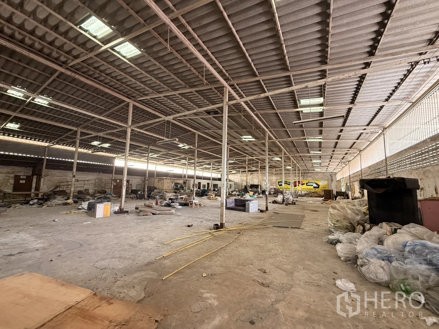 Warehouse for rent in Lam Luk Ka, Pathum Thani - Broad interior span with steel frame roof and stacked materials.