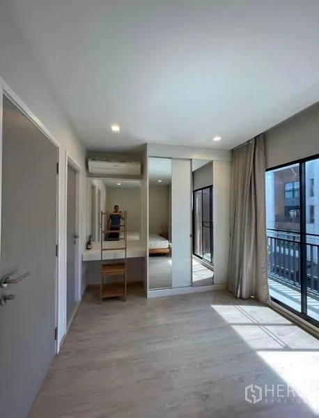 Townhouse for rent in Yan Nawa, Bangkok - Bedroom with built-in mirrored wardrobe, vanity, and sliding glass doors to the balcony.