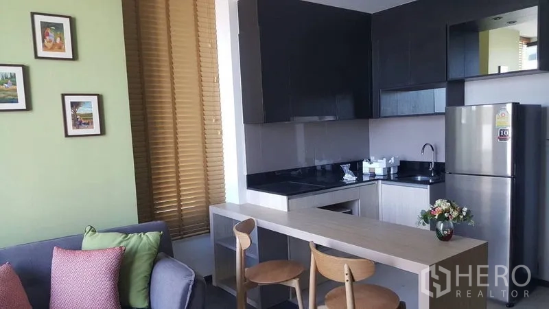Condominium for rent in Watthana, Bangkok - Open-plan kitchen with black cabinetry, breakfast bar and stools, stainless refrigerator and backsplash.