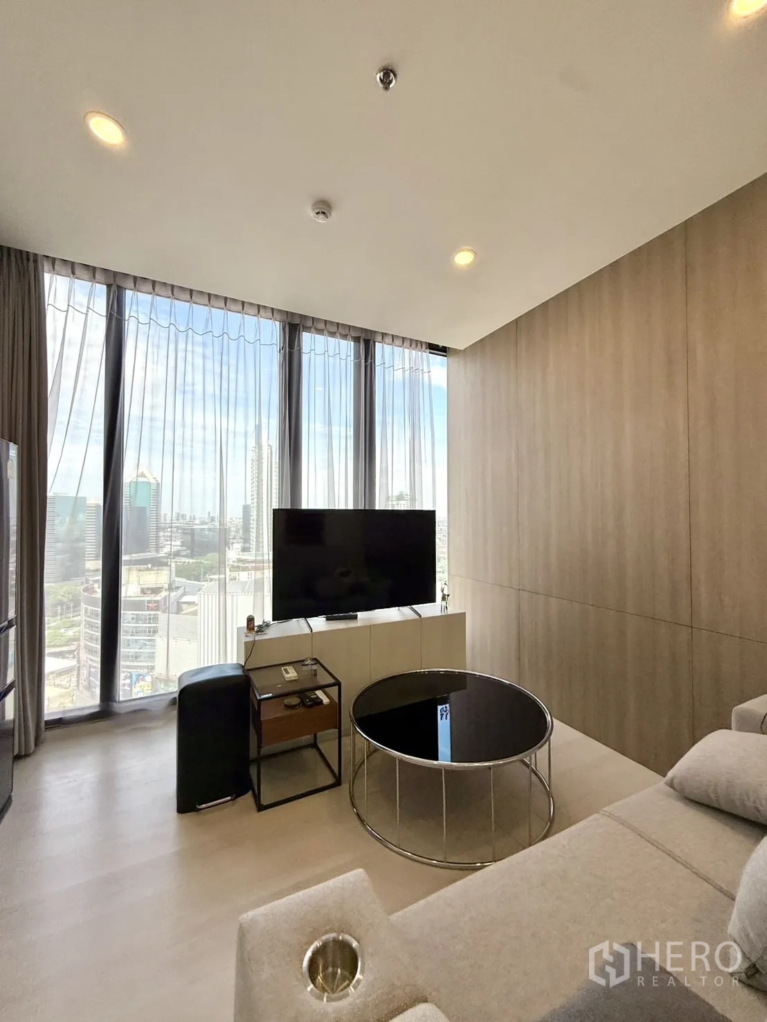 Condominium for sale in Chatuchak, Bangkok - Cozy lounge with sofa and round coffee table, curtain wall windows overlooking the city.