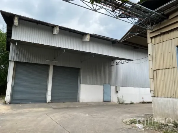 货栈 出租在Khlong Luang, Pathum Thani - 工业仓库正面，双卷帘门、侧门及宽阔混凝土车道，便于货车通行。
