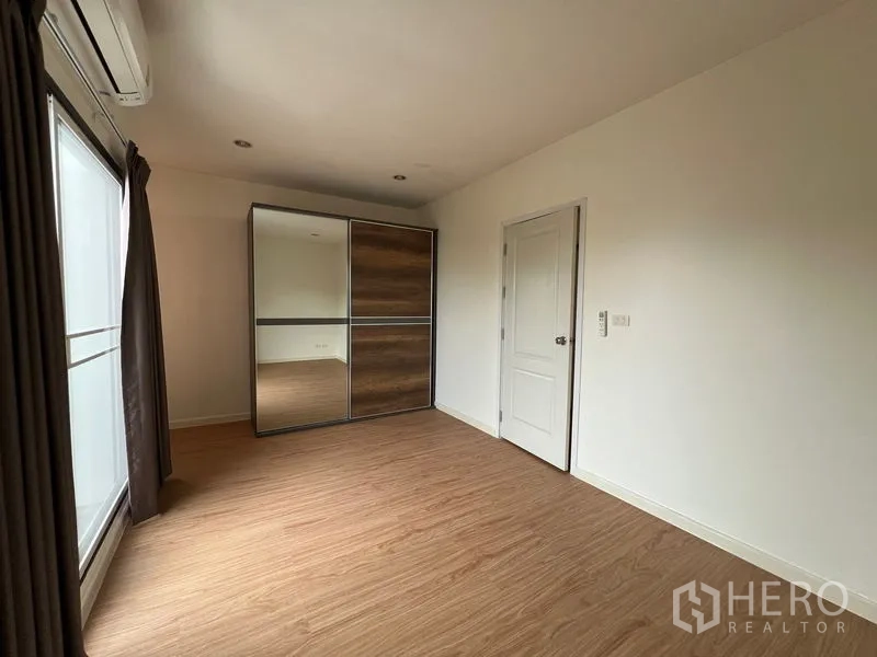 Townhouse for rent in Bang Kapi, Bangkok - Bedroom with mirrored sliding wardrobe and large window with curtains.