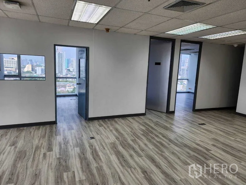 办公空间 出租在Phra Khanong, Bangkok - 开放式办公室内景，木纹地板、吊顶灯，带分隔房间与窗外城市景观。