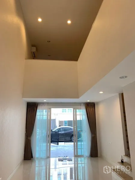 ทาวน์เฮาส์ ให้เช่าในBang Na, Bangkok - พื้นที่นั่งเล่นเปิดโล่ง ไฟดาวน์ไลท์ พร้อมประตูกระจกบานเลื่อนไปยังลานหน้าบ้านและที่จอดรถ