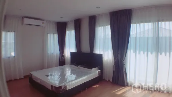Detached House for rent in Suan Luang, Bangkok - Sunlit master bedroom with large windows, sheer and blackout curtains, air conditioner, and wood flooring.