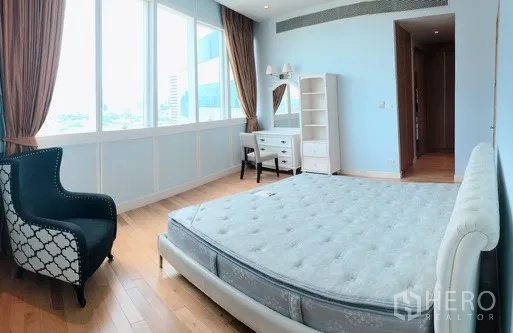 Condominium for rent or sale in Khlong Toei, Bangkok - Master bedroom with large windows, pastel blue walls, city outlook and an accent armchair.