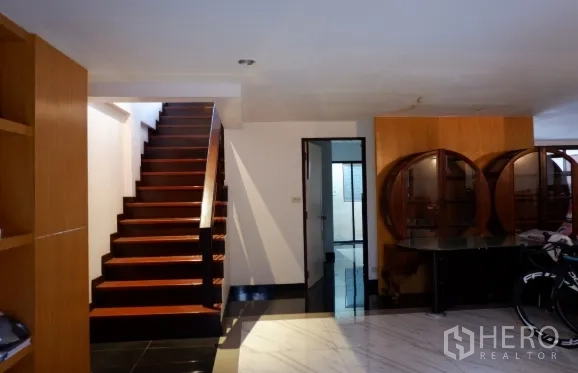 Townhouse for sale in Khlong Toei, Bangkok - Ground-floor hall with wooden staircase, built-in shelving and glossy tile flooring.