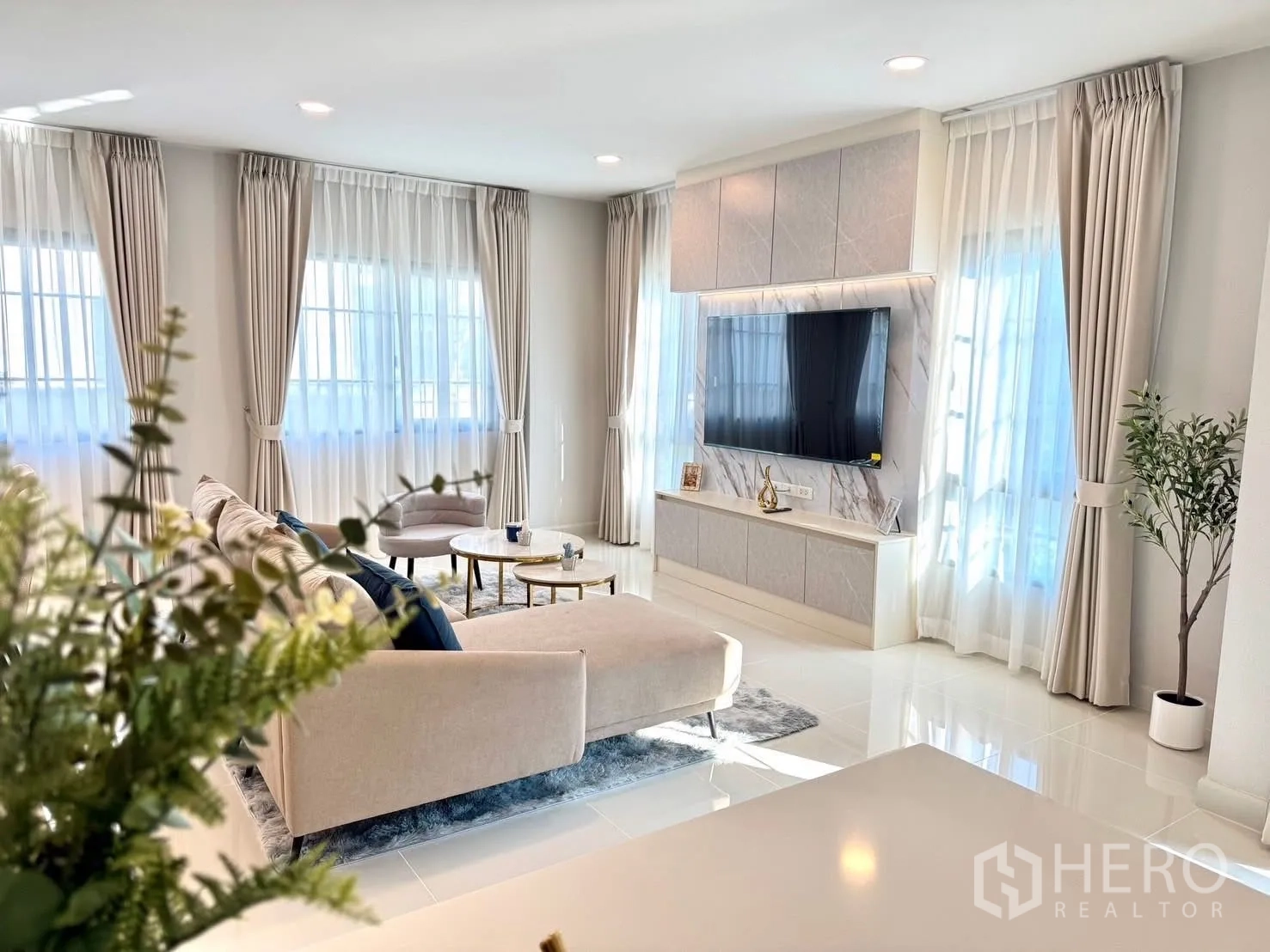 Detached House for rent in Bang Phli, Samut Prakan - Sunlit living room with tall windows, sheer drapes, and wall‑mounted TV.