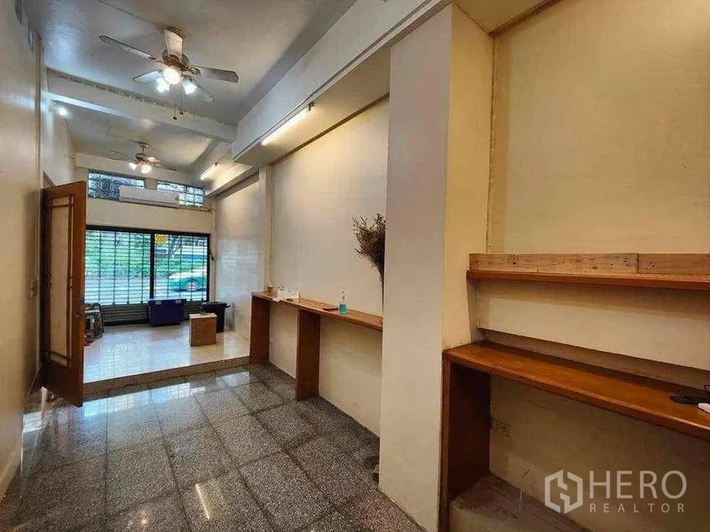 零售空间 出租在Khlong Toei, Bangkok - 开放式店铺空间，吊扇与木质展示架，面向玻璃店面。