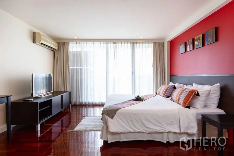 Condominium for rent in Bang Rak, Bangkok - Bright master bedroom with red accent wall, king bed, media console and sheer floor-to-ceiling curtains to the balcony.