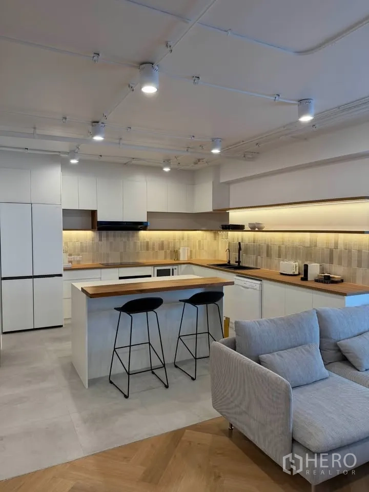 Condominium for rent in Watthana, Bangkok - Kitchen with peninsula breakfast bar and two stools under warm lighting.