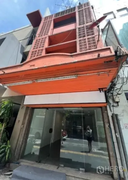 อาคารพาณิชย์ ให้เช่าในKhlong Toei, Bangkok - ด้านหน้าอาคารพาณิชย์ 3 ชั้น ติดถนน มีประตูม้วนสีส้มและกระจกหน้าร้าน.