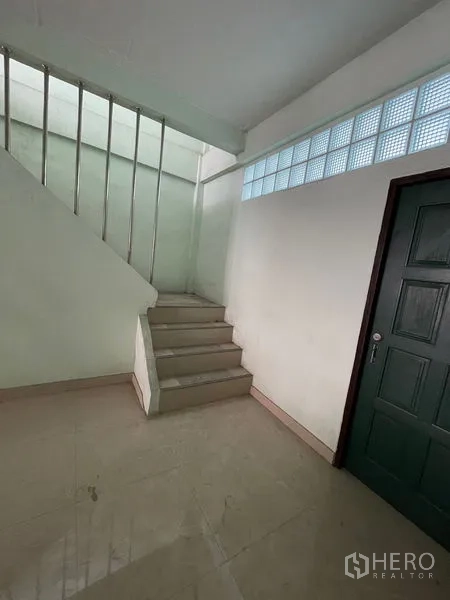 Shophouse for sale in Sathon, Bangkok - Landing area with staircase, glass-block sidelights and a dark green door.