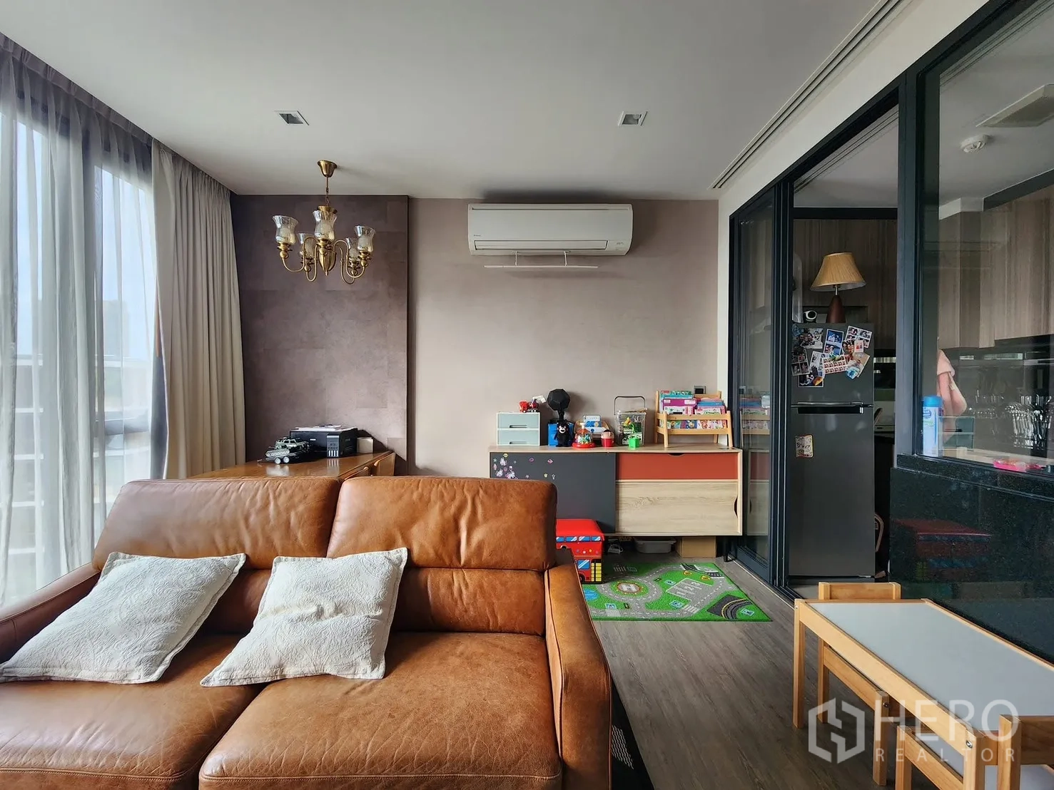 Condominium for rent in Watthana, Bangkok - Living area with chandelier, air conditioning, leather sofa, and sliding glass partition to the kitchen.