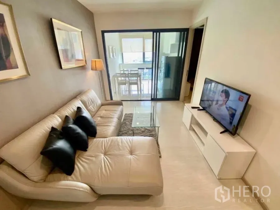 คอนโด ให้เช่าในKhlong Toei, Bangkok - มุมห้องนั่งเล่นหันหาโทรทัศน์และโซฟา กั้นด้วยผนังกระจกไปยังห้องครัว โทนสีเรียบ