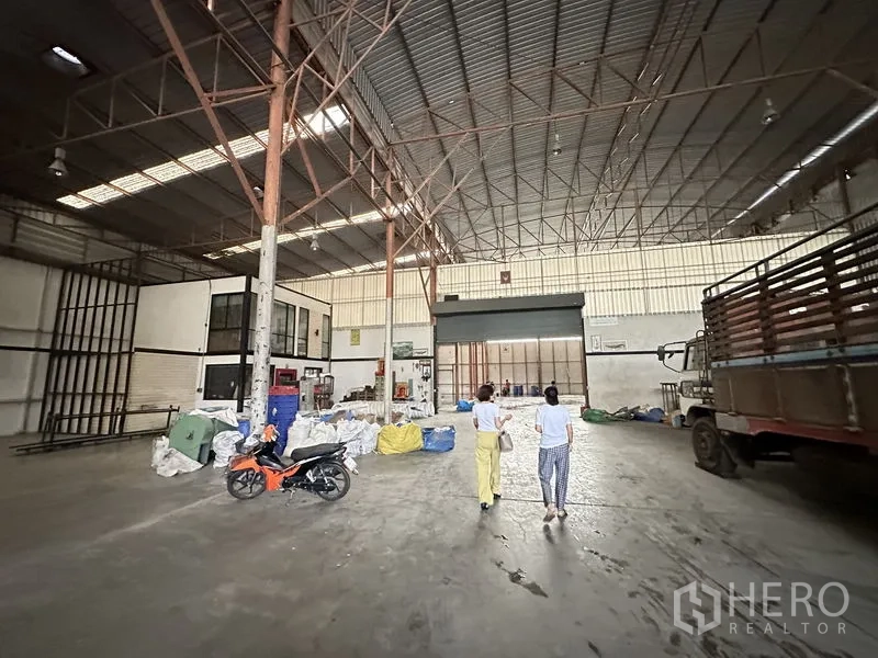 工厂 出租在Bang Bua Thong, Nonthaburi - 大跨仓库，钢柱林立，地面堆放材料与卷帘门。