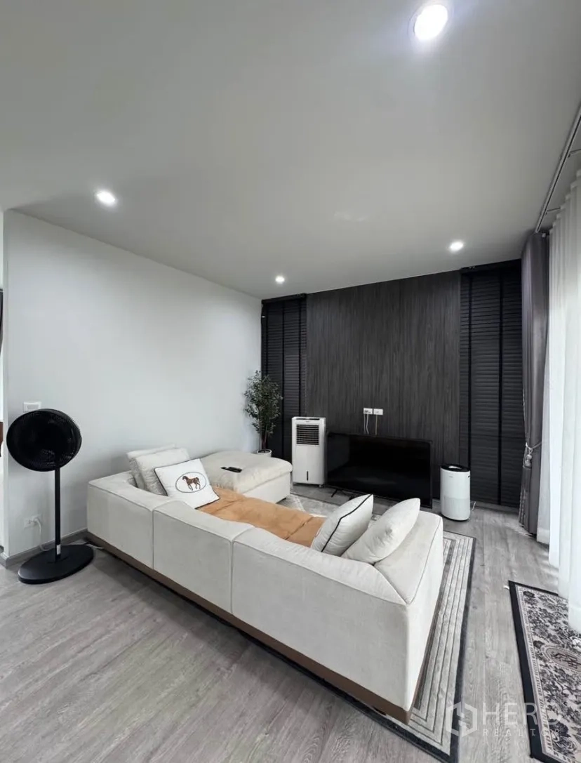 บ้านเดี่ยว for rent or sale in Lat Krabang, Bangkok - ห้องนั่งเล่นสมัยใหม่ โซฟาเข้ามุม เพดานดาวน์ไลท์ ผนังลายไม้สีเข้ม และชั้นวางทีวี