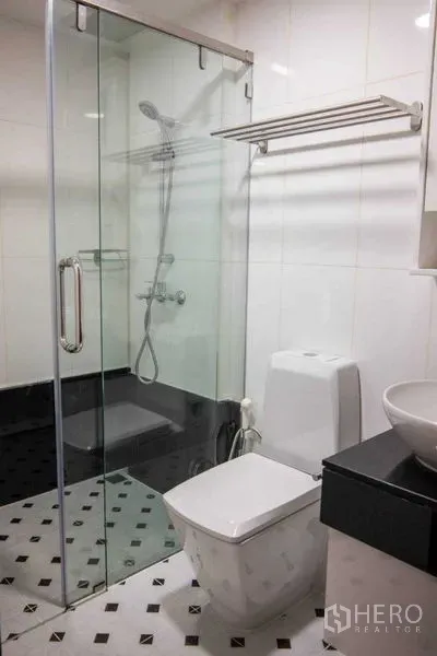 Condominium for rent in Pathum Wan, Bangkok - White-tiled bathroom with glass-enclosed shower, toilet and vessel sink on black vanity