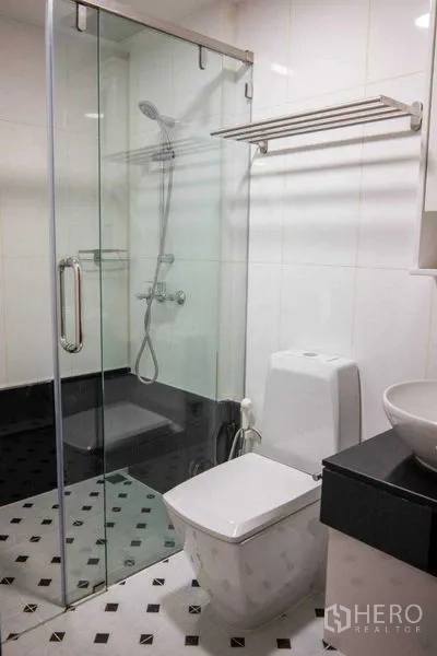 Condominium for rent in Pathum Wan, Bangkok - White-tiled bathroom with glass-enclosed shower, toilet and vessel sink on black vanity