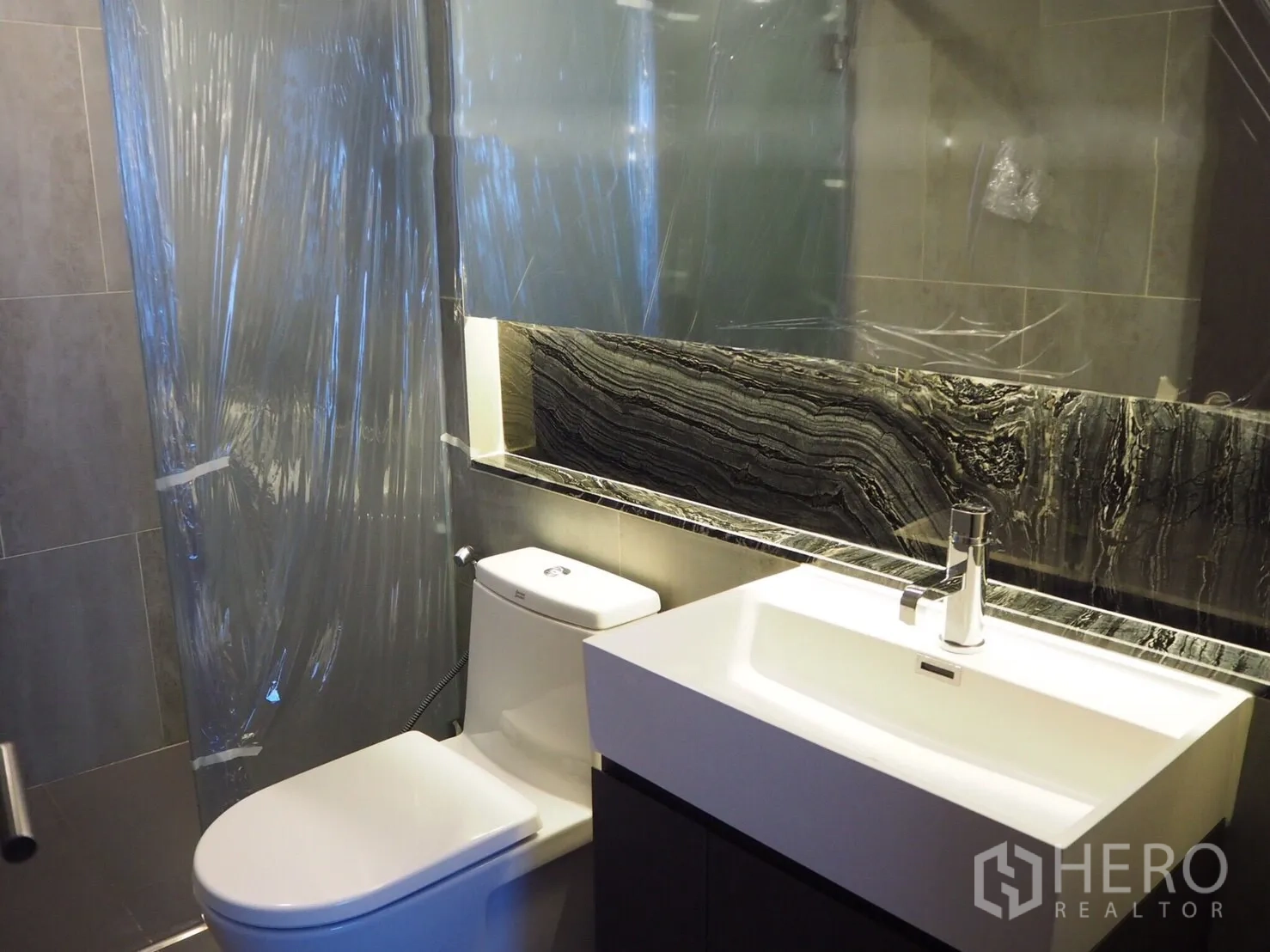 Condominium for rent in Khlong Toei, Bangkok - Contemporary bathroom with stone backsplash, large mirror, toilet and square basin.