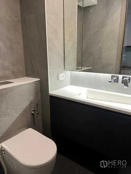 Condominium for sale in Huai Khwang, Bangkok - Modern bathroom with large mirror, vanity storage and toilet.
