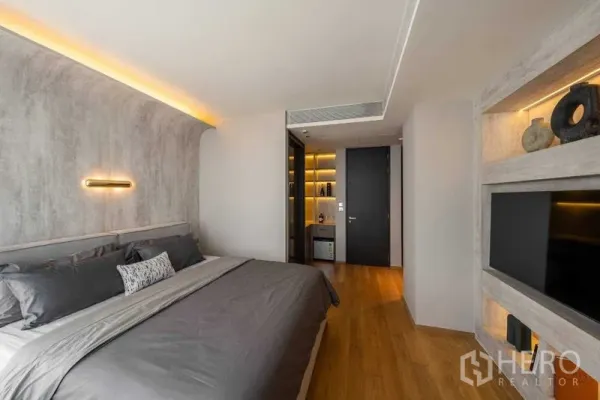 คอนโด ขายในKhlong Toei, Bangkok - ห้องนอนหลัก ผนังโค้งลุคปูนเปลือย ไฟซ่อน เตียงคิงไซซ์ และชั้นวางทีวีบิลต์อิน