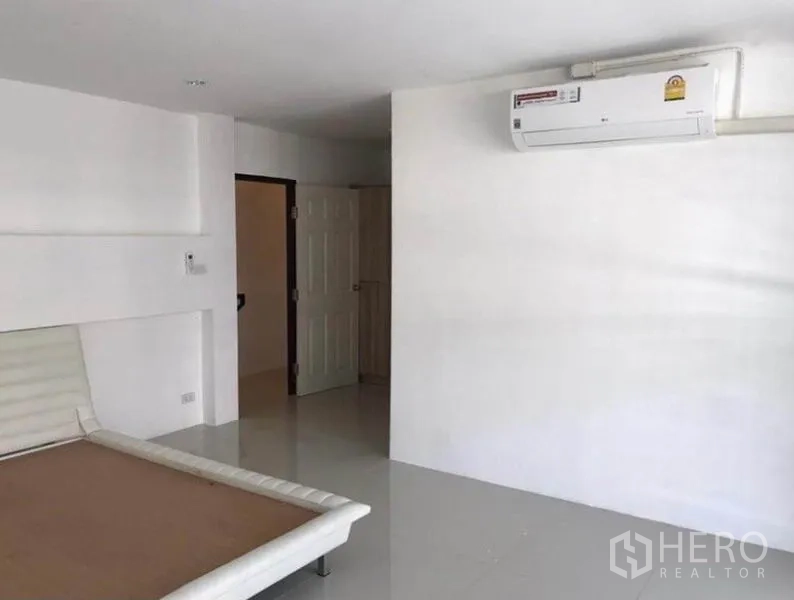 Townhouse for rent in Wang Thonglang, Bangkok - Large bedroom with air conditioner and built-in bed base against white walls.